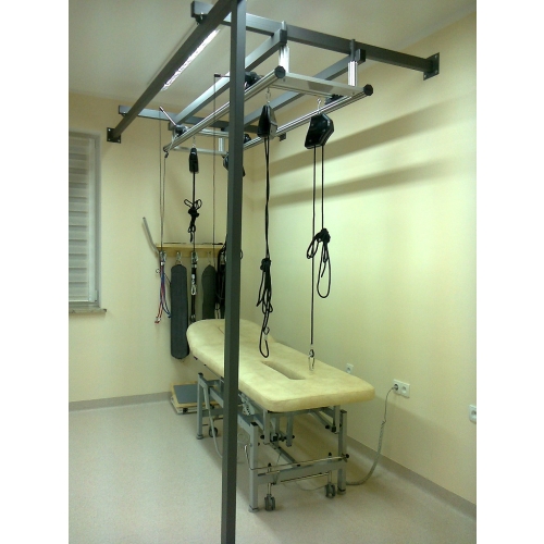 Konstrukcja Kinesis do Sling Therapy, z systemem lin i podwieszeń nad stołem rehabilitacyjnym.