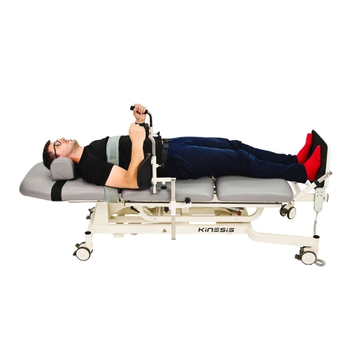 Pacjent na stole pionizacyjnym BLUEFORD w pozycji leżącej, z pasami i uchwytami stabilizującymi.